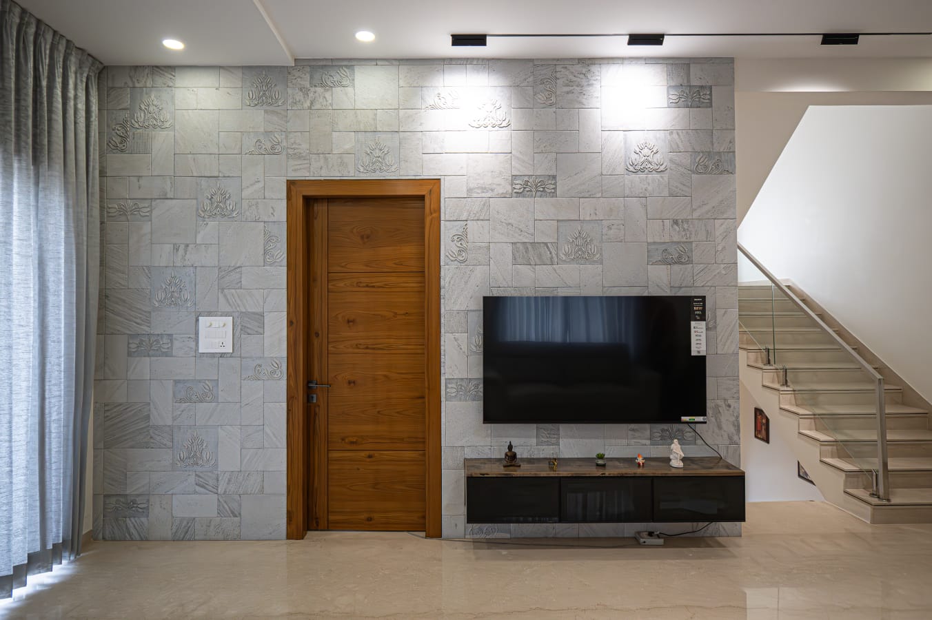 Mounted television screen on fluted grey architectural stone wall with floating console beside staircase