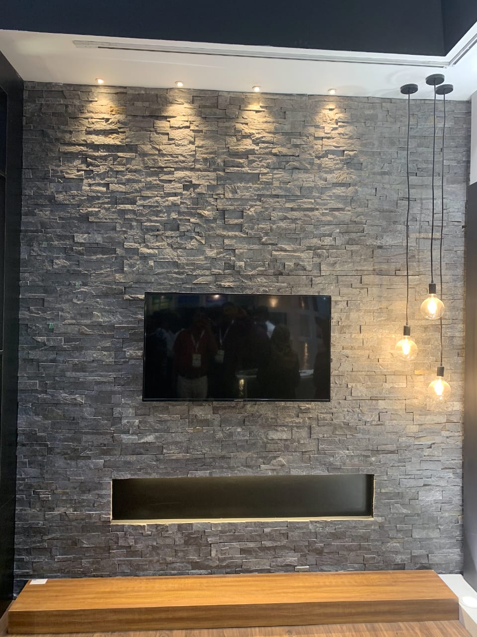 Entertainment media wall featuring mounted television on stacked stone ledger cladding with fireplace cutout